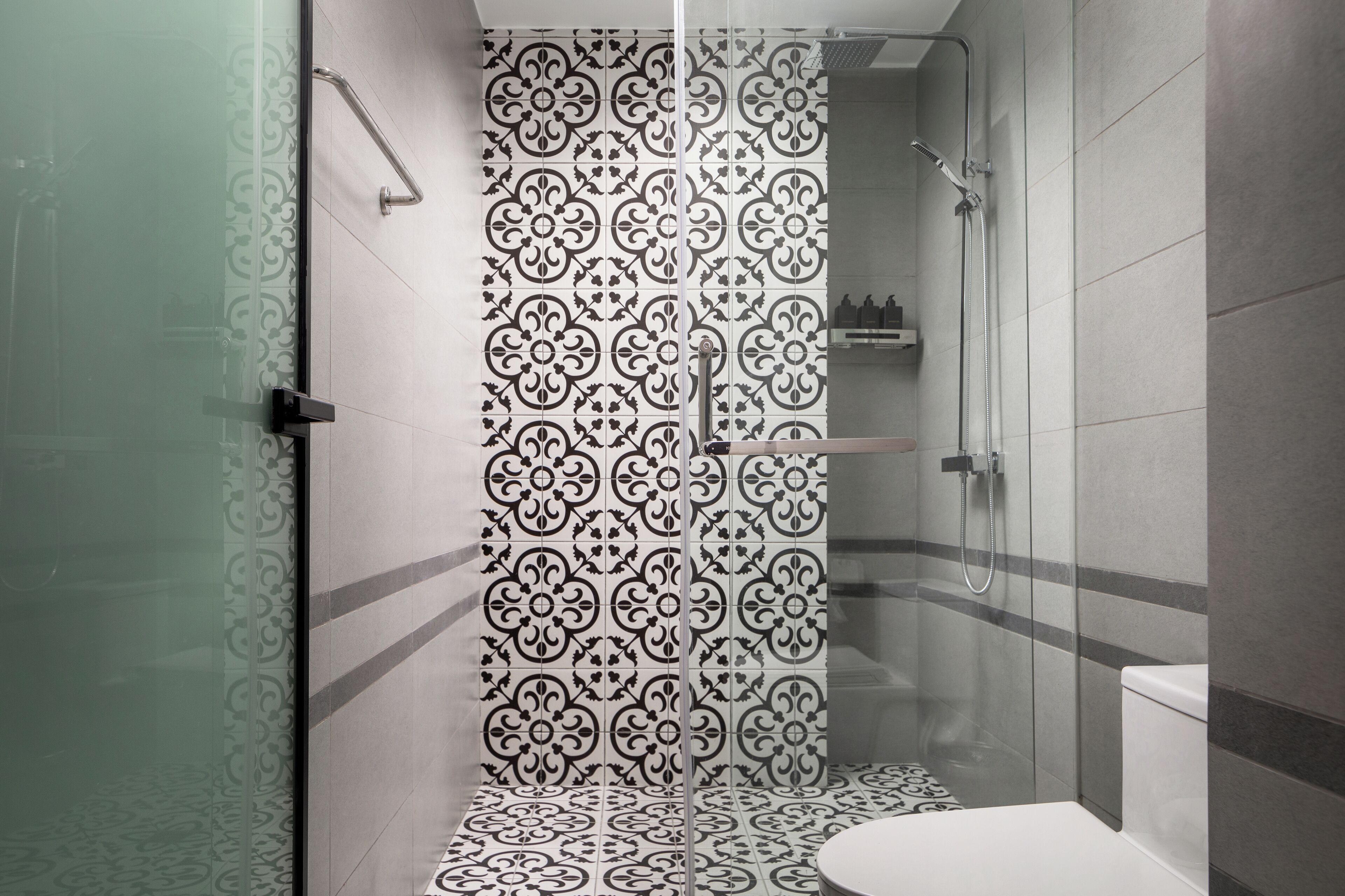 Un bany modern amb una cabina de dutxa de vidre, rajoles amb dibuixos i un vàter.