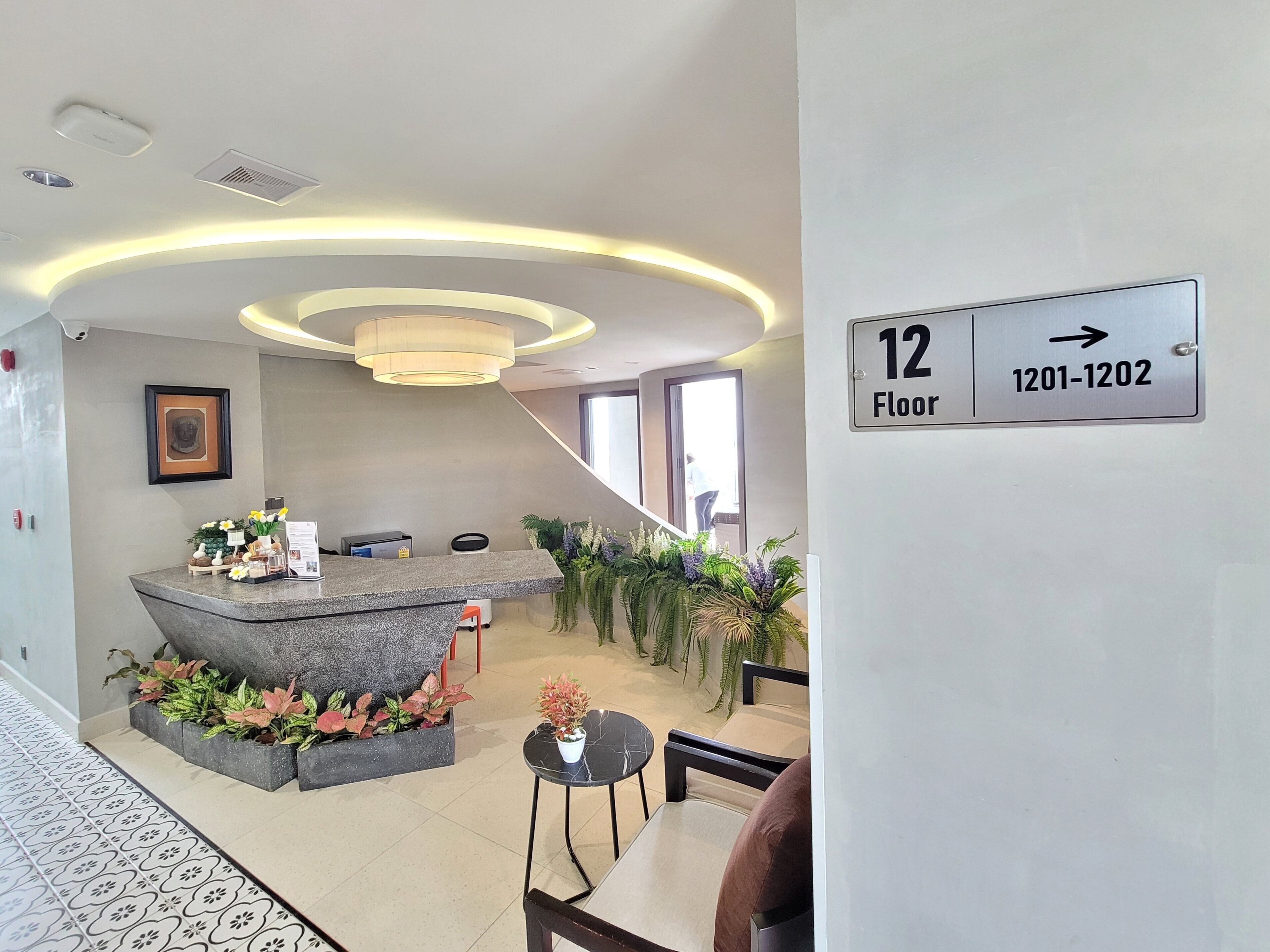 A modern reception area with a marble counter, potted plants, and a sign indicating floor 12.