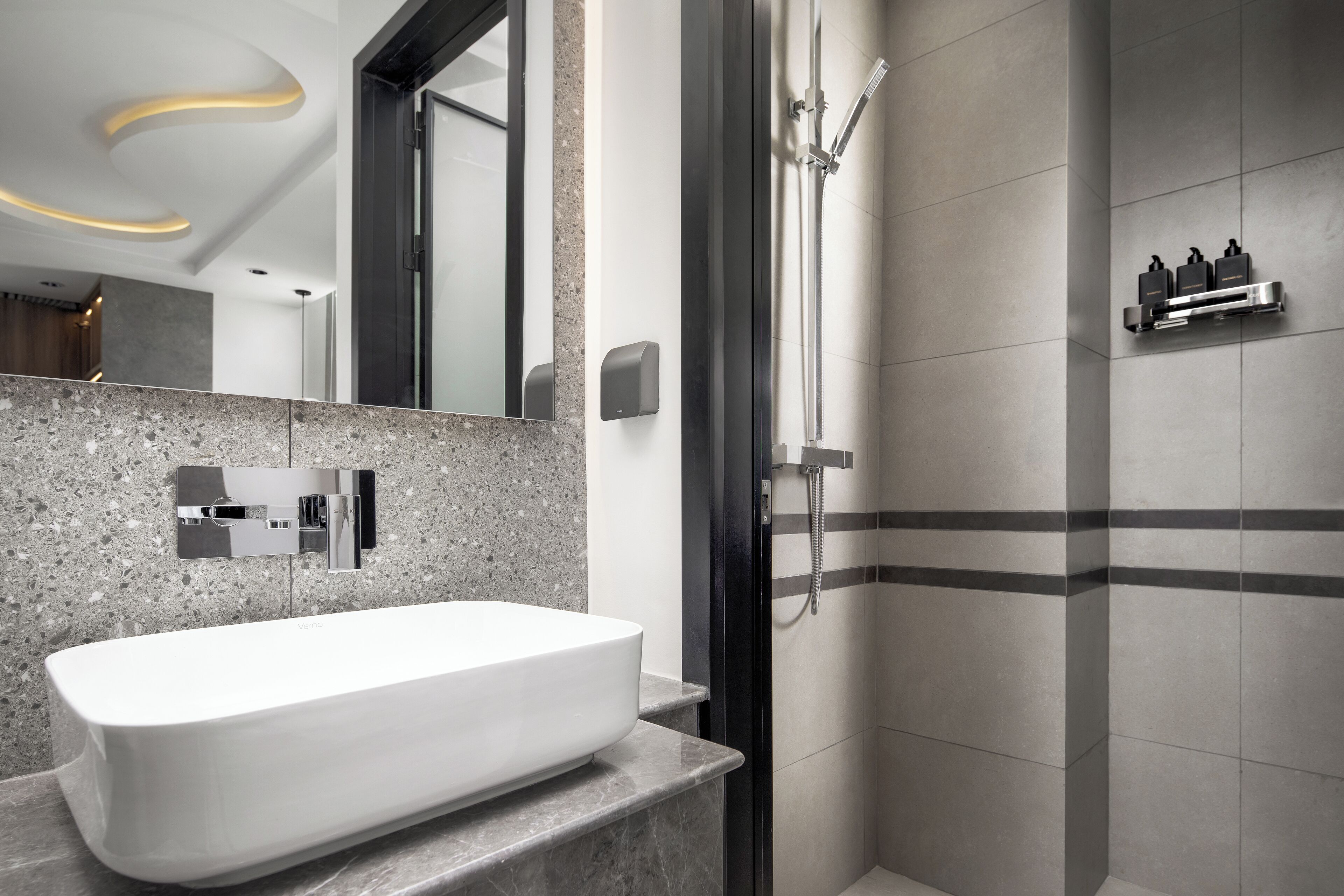 Un baño moderno con un lavamanos grande blanco, una ducha con cabezal de ducha de mano y un dispensador de jabón de pared.