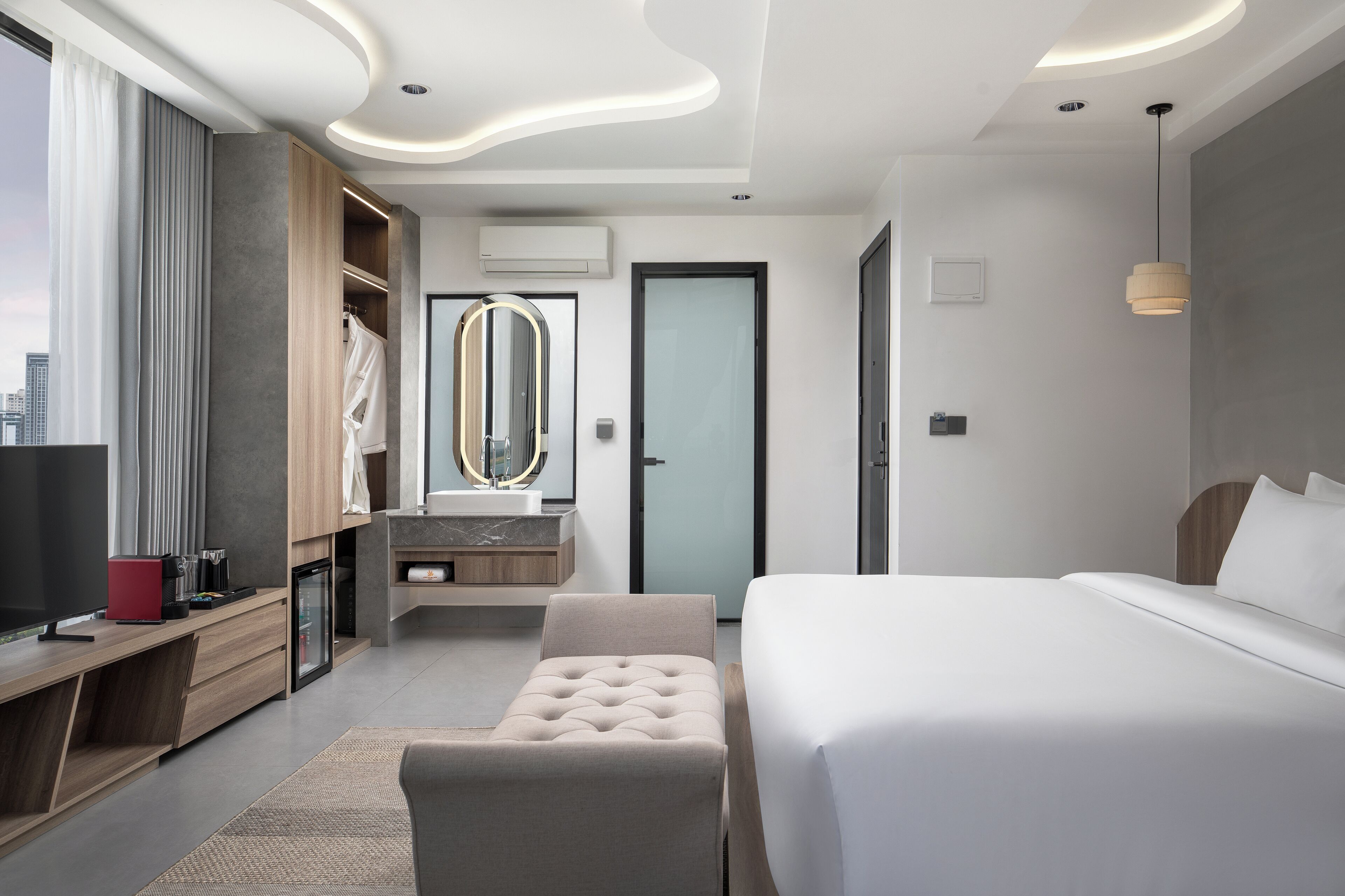Una habitación de hotel moderna con una cama grande, una zona de estar, un tocador con espejo y vistas a la ciudad.