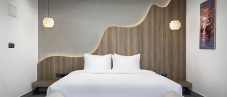 A modern bedroom with a large bed, two pendant lights, a wooden headboard, and a painting on the wall.