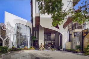 Una entrada de hotel moderna con puertas de cristal, un letrero del Hotel Chaiya Palace y un bar Sky visible.