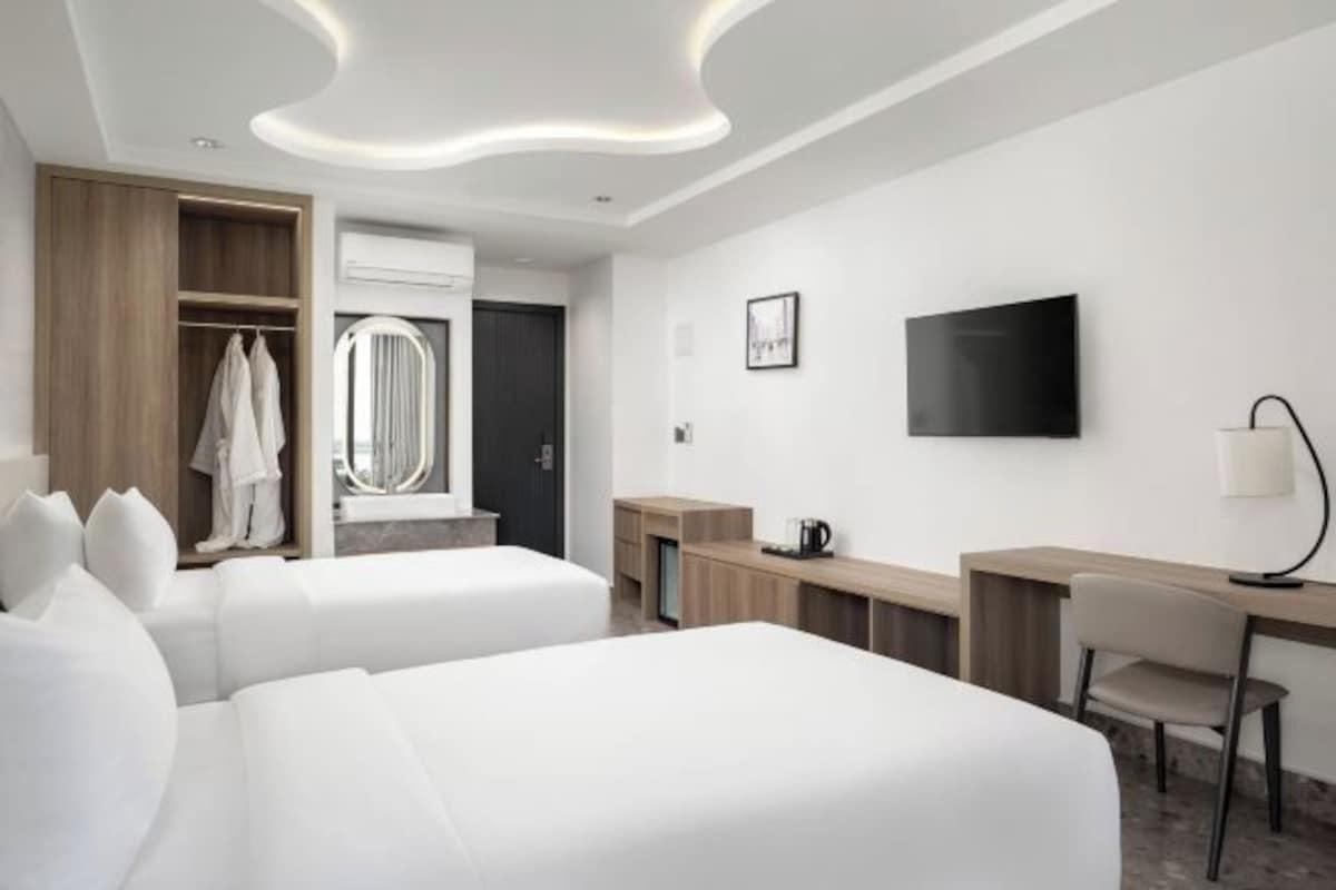 Una habitación de hotel moderna con dos camas, un escritorio, una silla, un televisor y un armario.