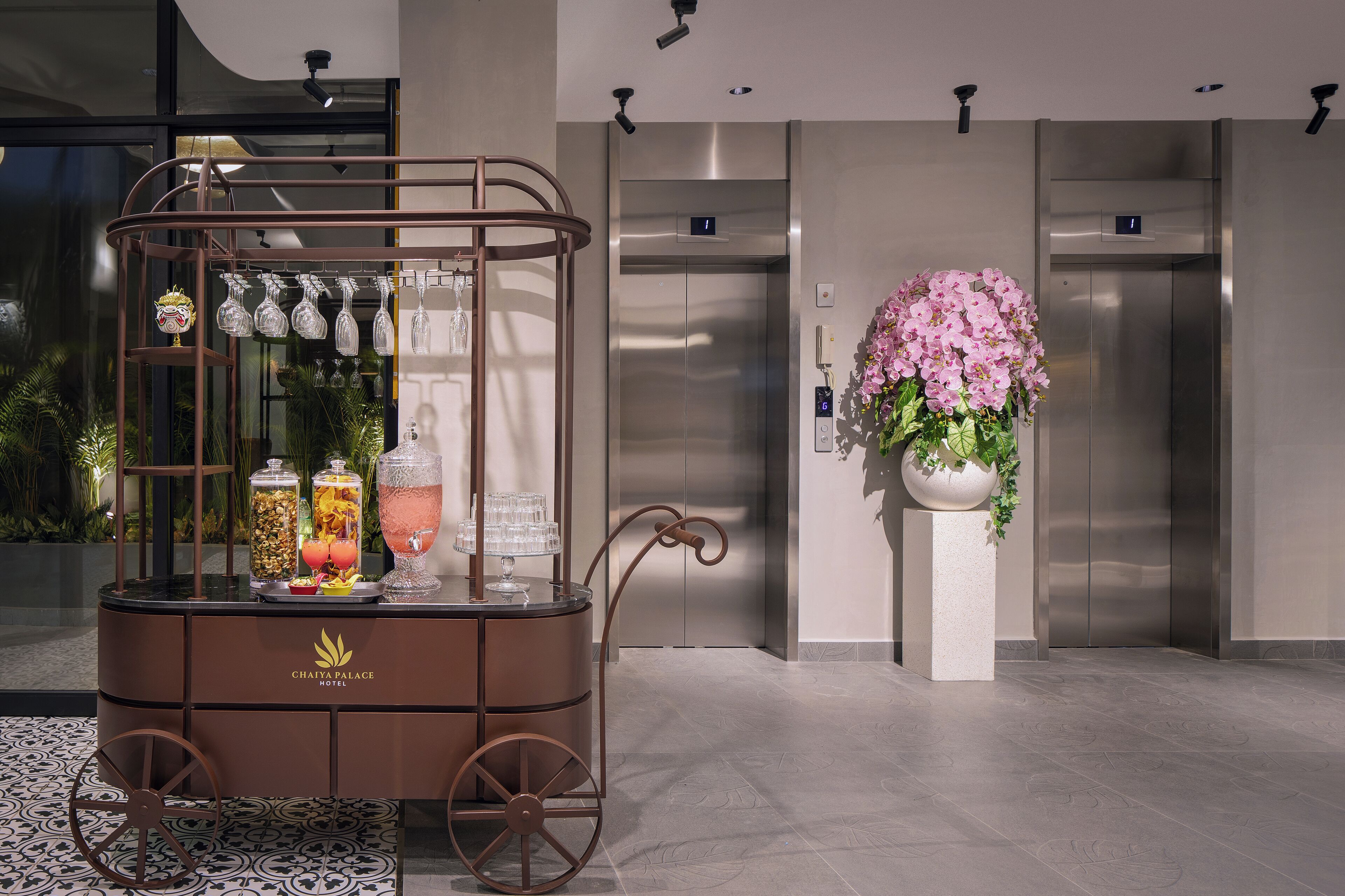 A modern hotel lobby with a stationary bar cart, an elevator, and a large potted plant.