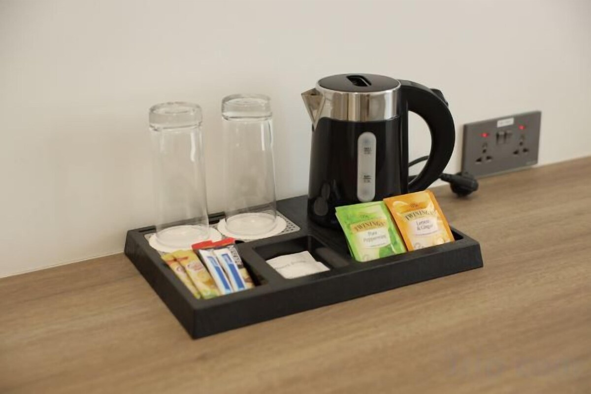Una estación de café con una tetera, dos jarrones de vidrio y sobres de café y crema.