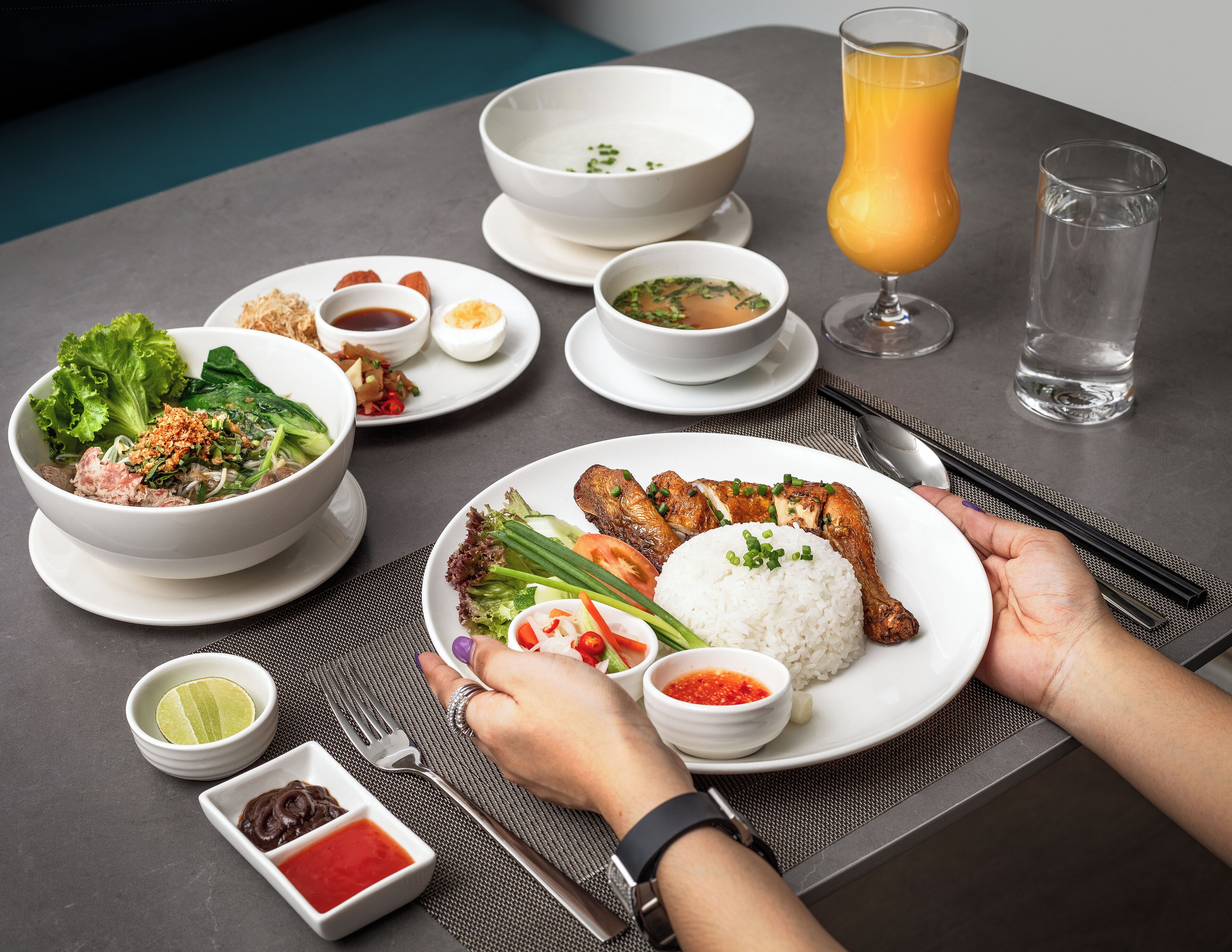 A table set with various dishes including a bowl of soup, a plate with rice and meat, and a glass of orange juice.