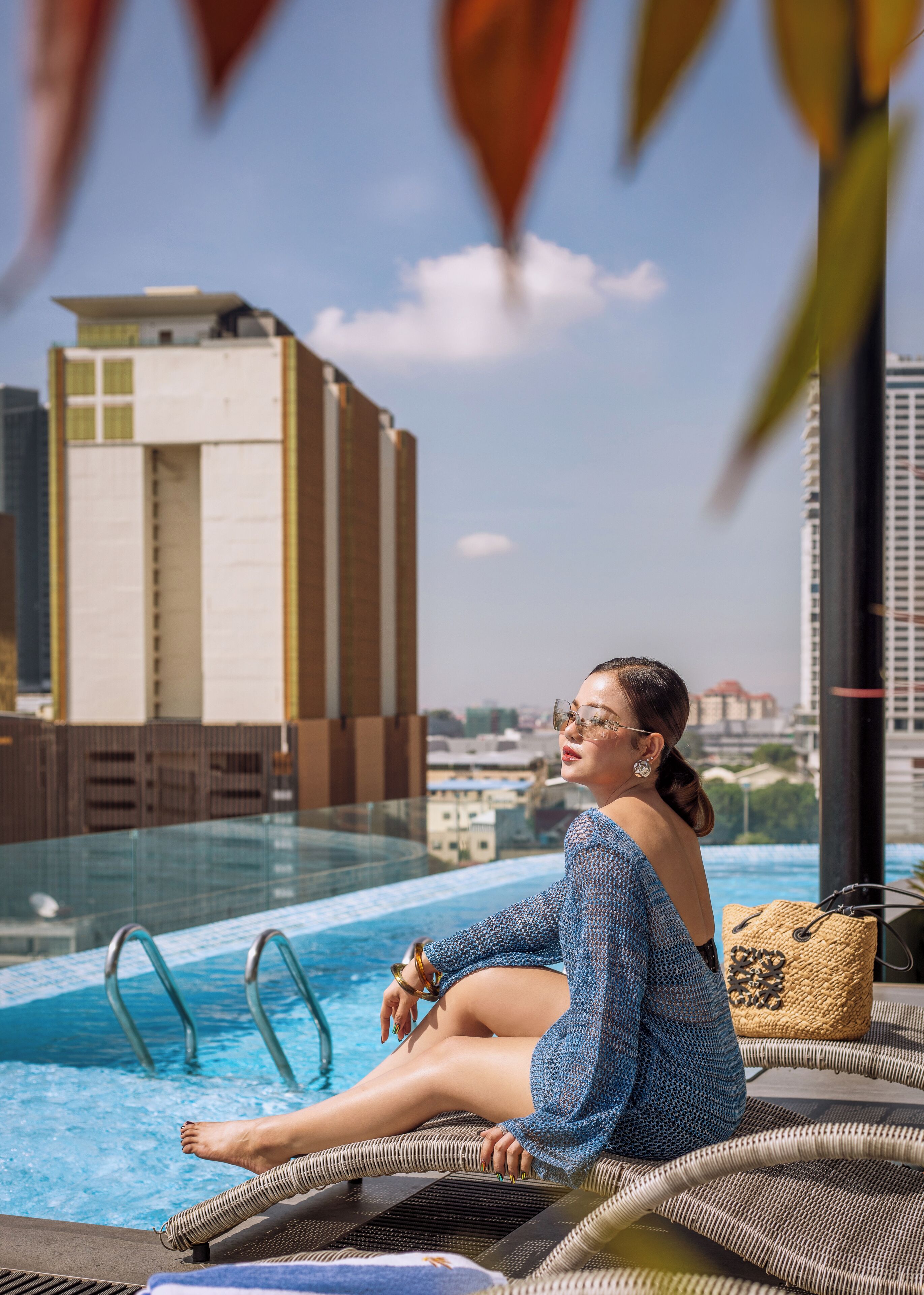A person sitting by a pool with a view of a tall building in the background.