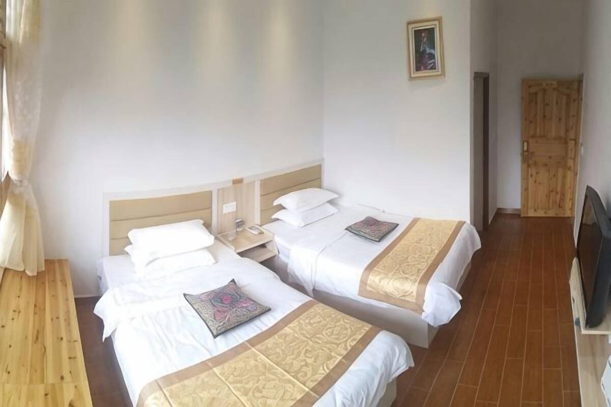 Een hotelkamer met twee bedden, een houten bankje, een televisie en een deur.