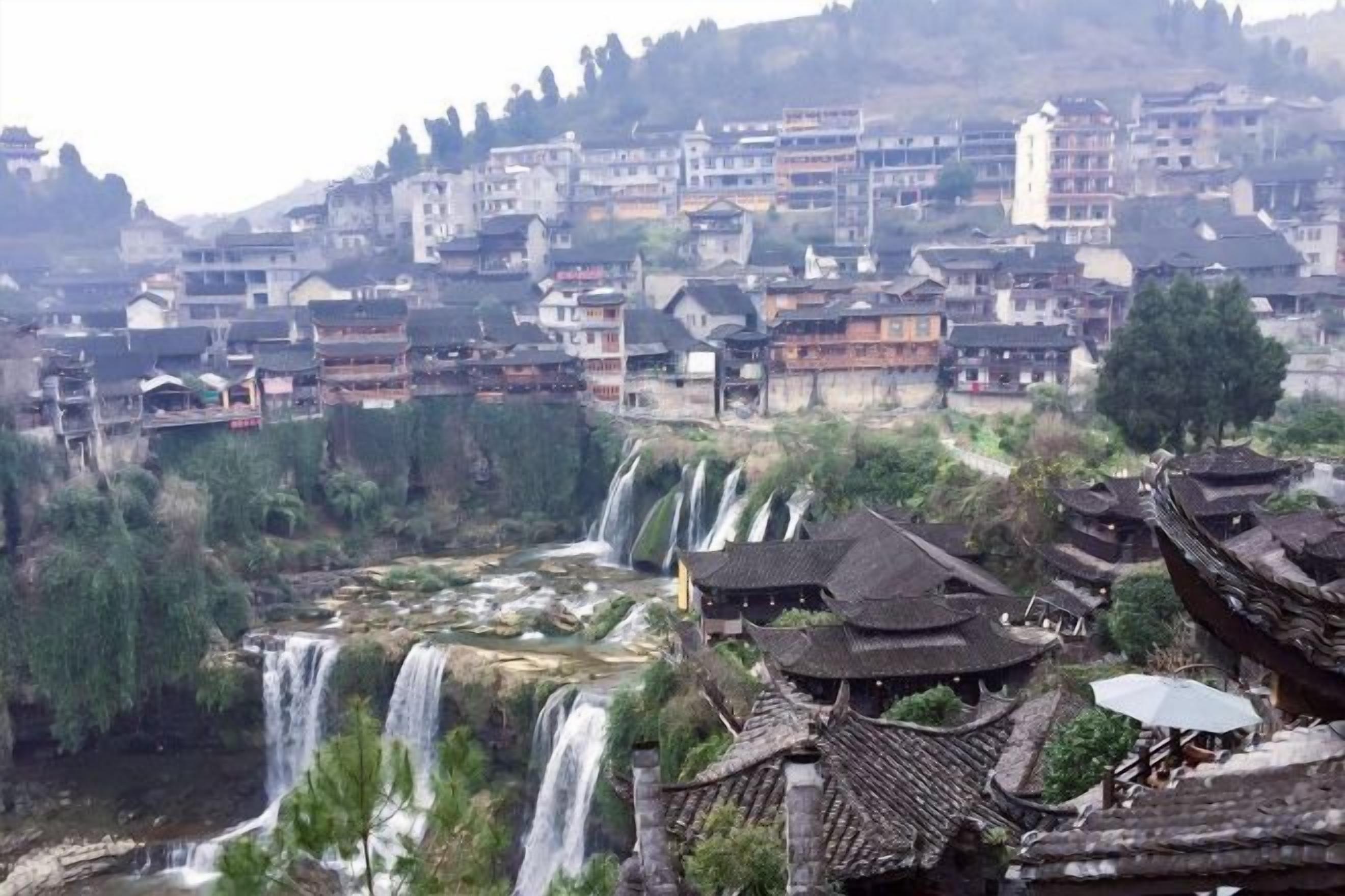 A traditional village with multiple waterfalls, traditional architecture, and a river.