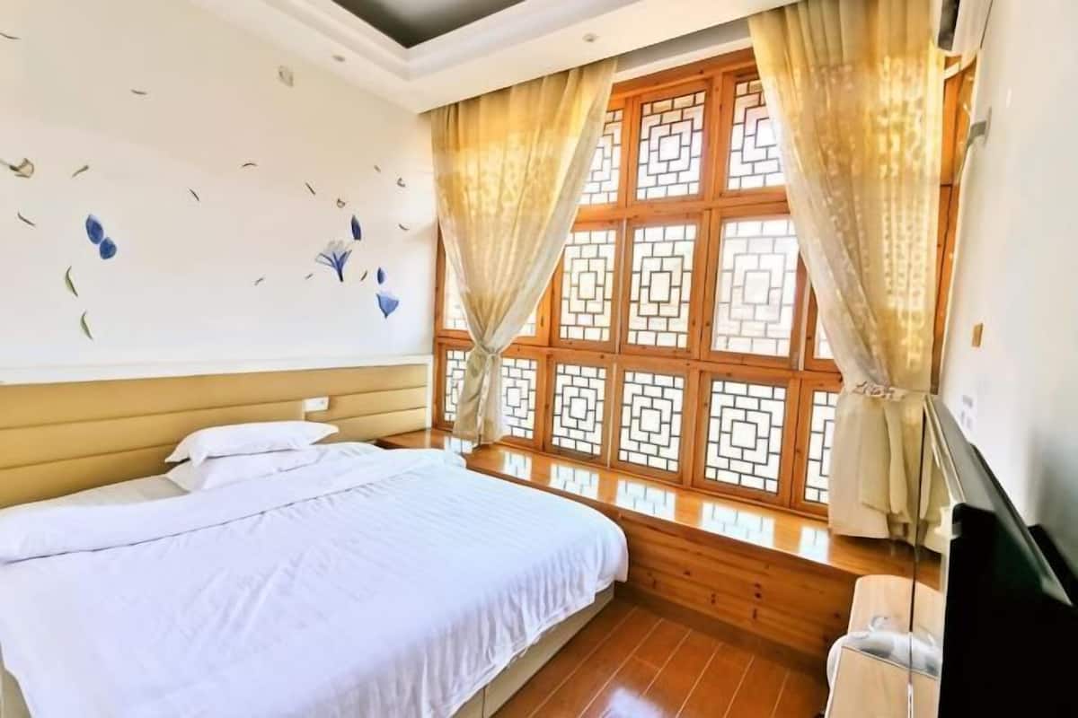 Een slaapkamer met een bed, een televisie, een raam met gordijnen en een decoratieve wand.
