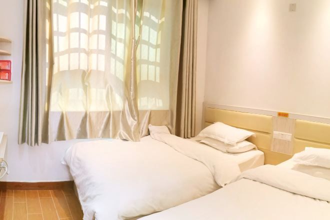 Une chambre d’hôtel avec deux lits, une fenêtre avec des rideaux, une tête de lit et un luminaire fixé au mur.