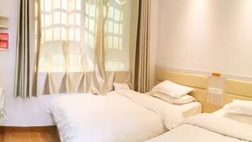 Une chambre d’hôtel avec deux lits, une fenêtre avec des rideaux, une tête de lit et un luminaire fixé au mur.