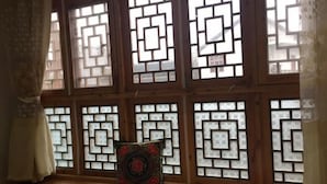 Een kamer met houten vloer, een decoratief kussen en een raam met geometrische patronen.