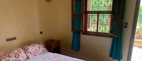 A bedroom with a bed, a nightstand, a window with curtains, and a wall-mounted light fixture.