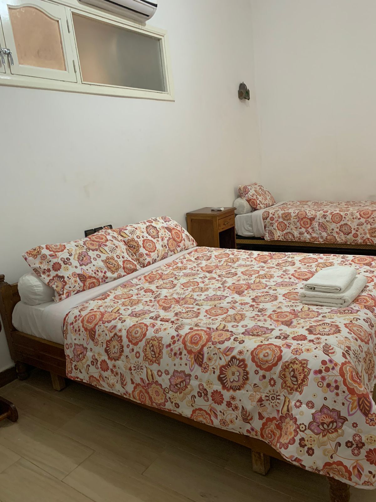 Un dormitorio con dos camas, cada una con ropa de cama de motivos florales, cabeceros de madera y mesitas de noche.