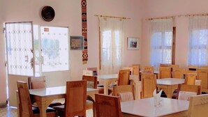 Un comedor con mesas y sillas de madera, baldosas de piso estampadas y ventanas con cortinas.