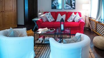 Una sala de estar con un sofá rojo, sillones blancos, una mesa de centro de vidrio y un aparador de madera.