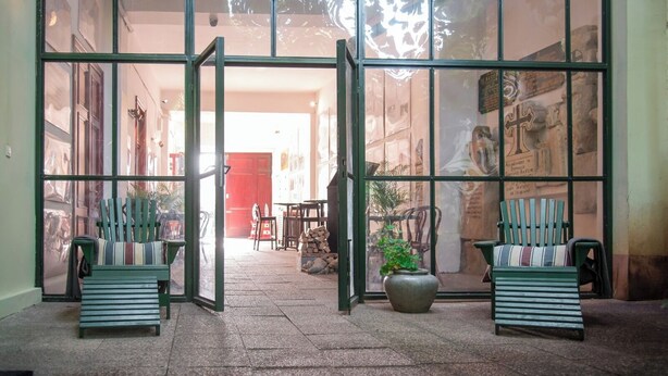 A building entrance with a glass door, a red door in the background, and two green benches outside. - Ratiu House (Turda)