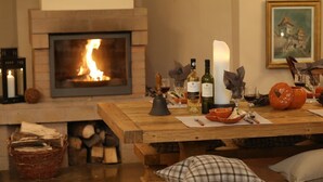 A cozy room with a fireplace, a dining table set with wine glasses, bottles, and pumpkins. - Ratiu House (Turda)