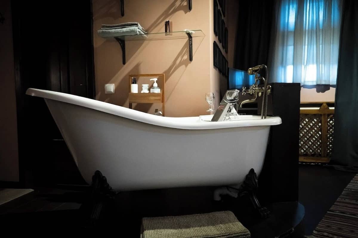 A bathroom with a freestanding bathtub, a glass shelf with toiletries, and a window with curtains.