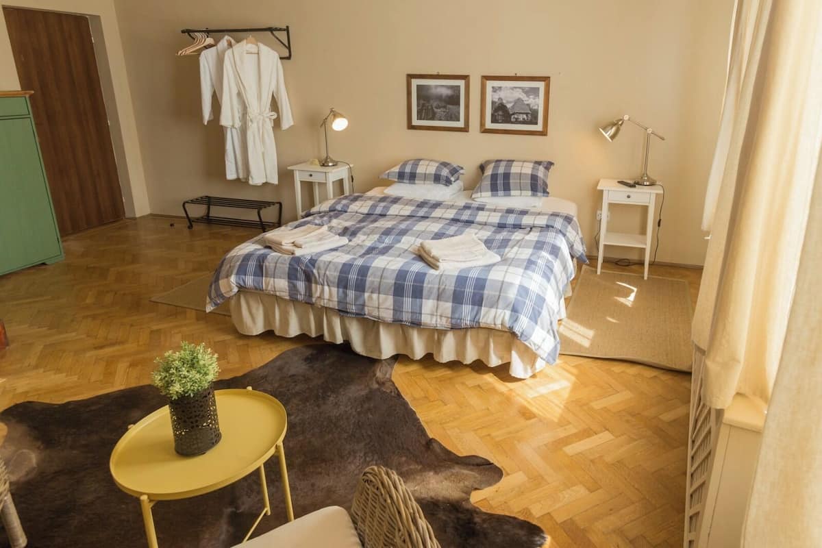 A bedroom with a large bed, two bedside tables with lamps, a wooden floor, a fur rug, and a small table with a plant.