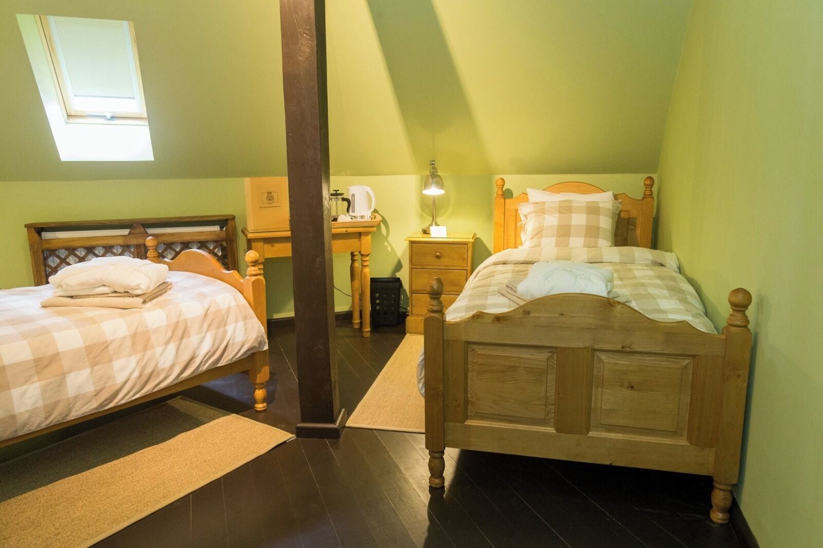 Ein Schlafzimmer mit zwei Holzbett, einem Schreibtisch, einem Stuhl, einem Nachttisch, einer Lampe und einem Fenster.
