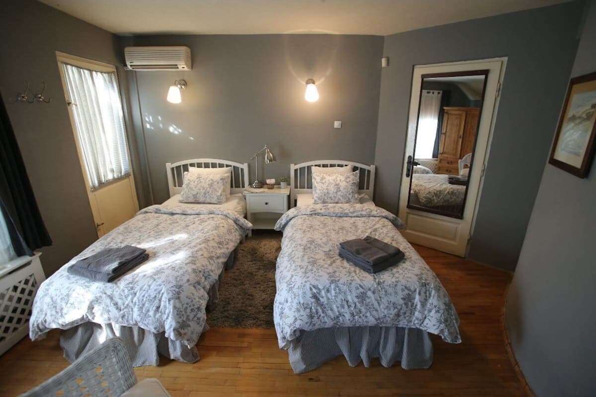 A bedroom with two single beds, a bedside table with a lamp, a radiator, and a window with blinds.