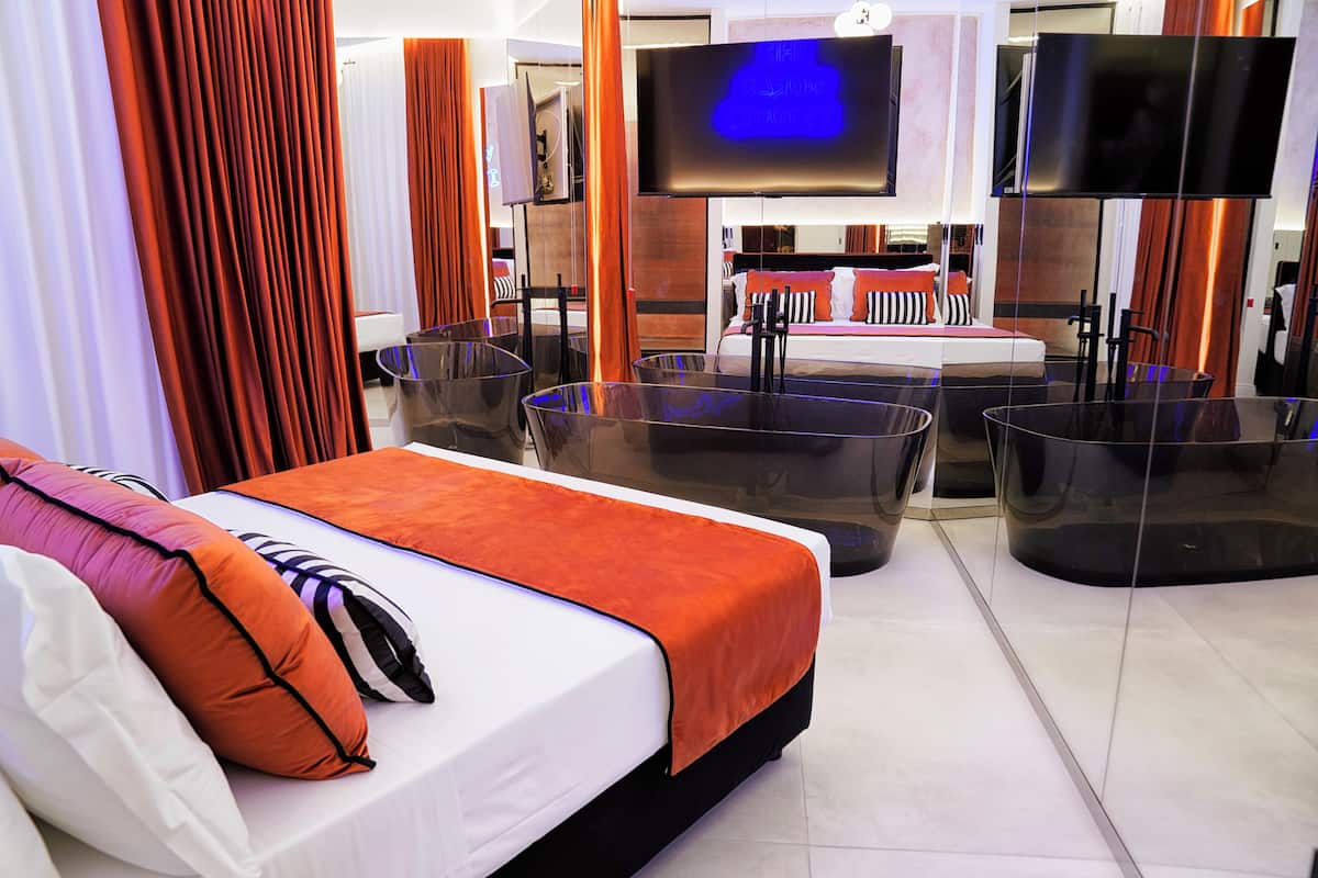 A modern hotel room with a large bed, a flat-screen TV, and a seating area with glass tables.