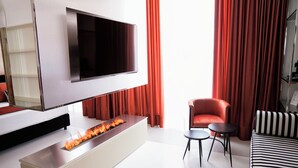 Una sala de estar moderna con un televisor de pantalla plana montado en la pared, una chimenea empotrada, un sillón rojo, un sofá a rayas y una mesita auxiliar pequeña.