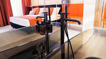 Et moderne hotelværelse med en stor seng, en brusekabine i glas og et synligt badeværelsesbord med toiletartikler.