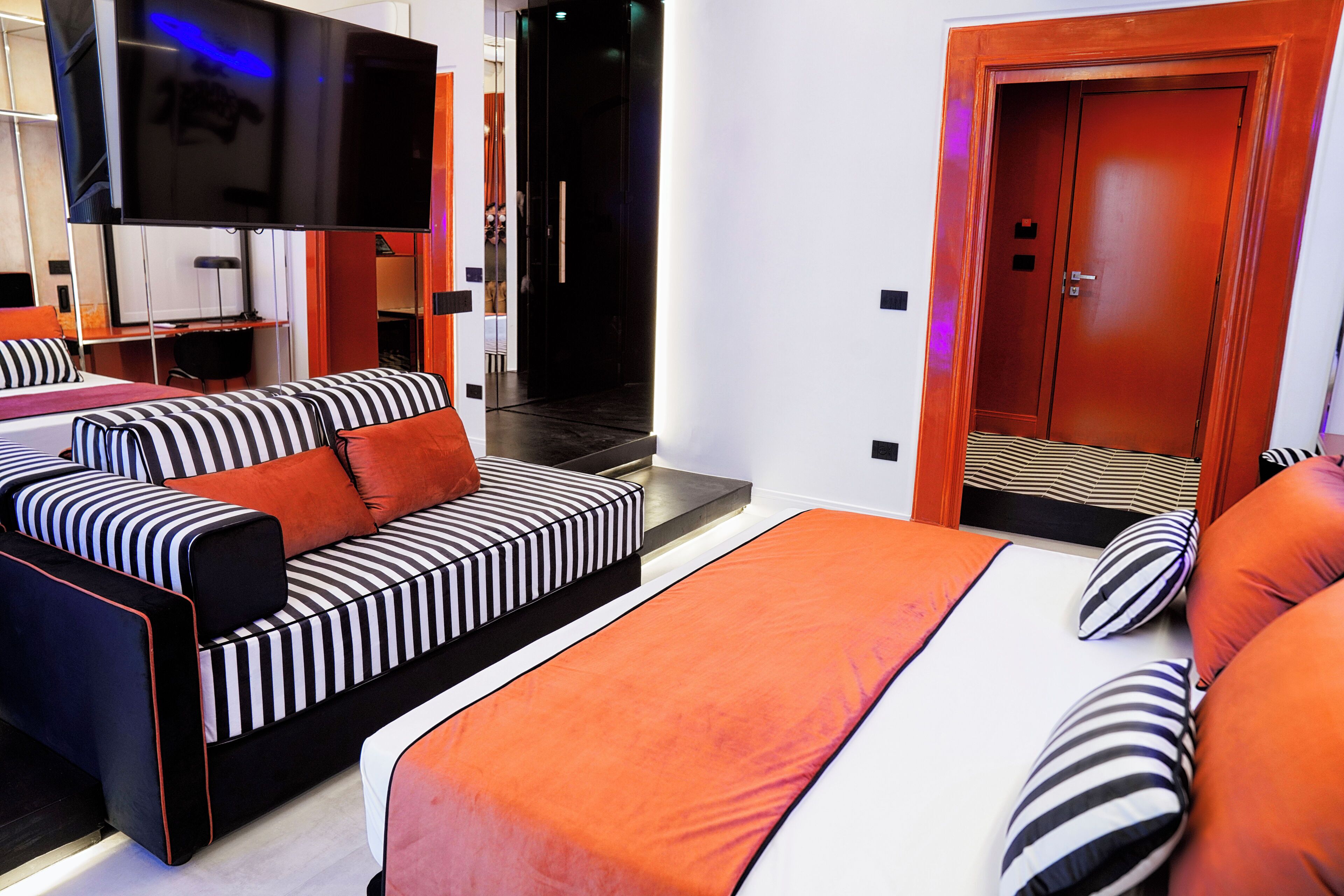 A modern hotel room with a large bed, a sofa, a TV, and a door.
