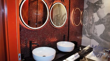 A modern bathroom with two white sinks, a black countertop, and a mirror with a circular frame.