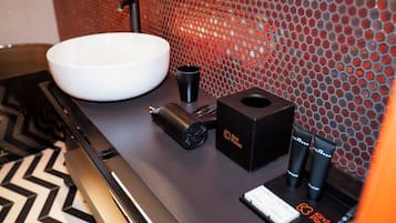 A modern bathroom with a large white sink, a black handheld showerhead, and two black bottles labeled 'kind places' on a black countertop.