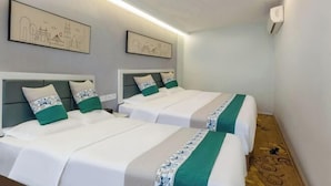 A hotel room with two beds, each with a green and white bedspread and matching pillows. There are two framed cityscape artworks on the wall above the beds. - Cornwall Hotel Chaozhou (Chaozhou)