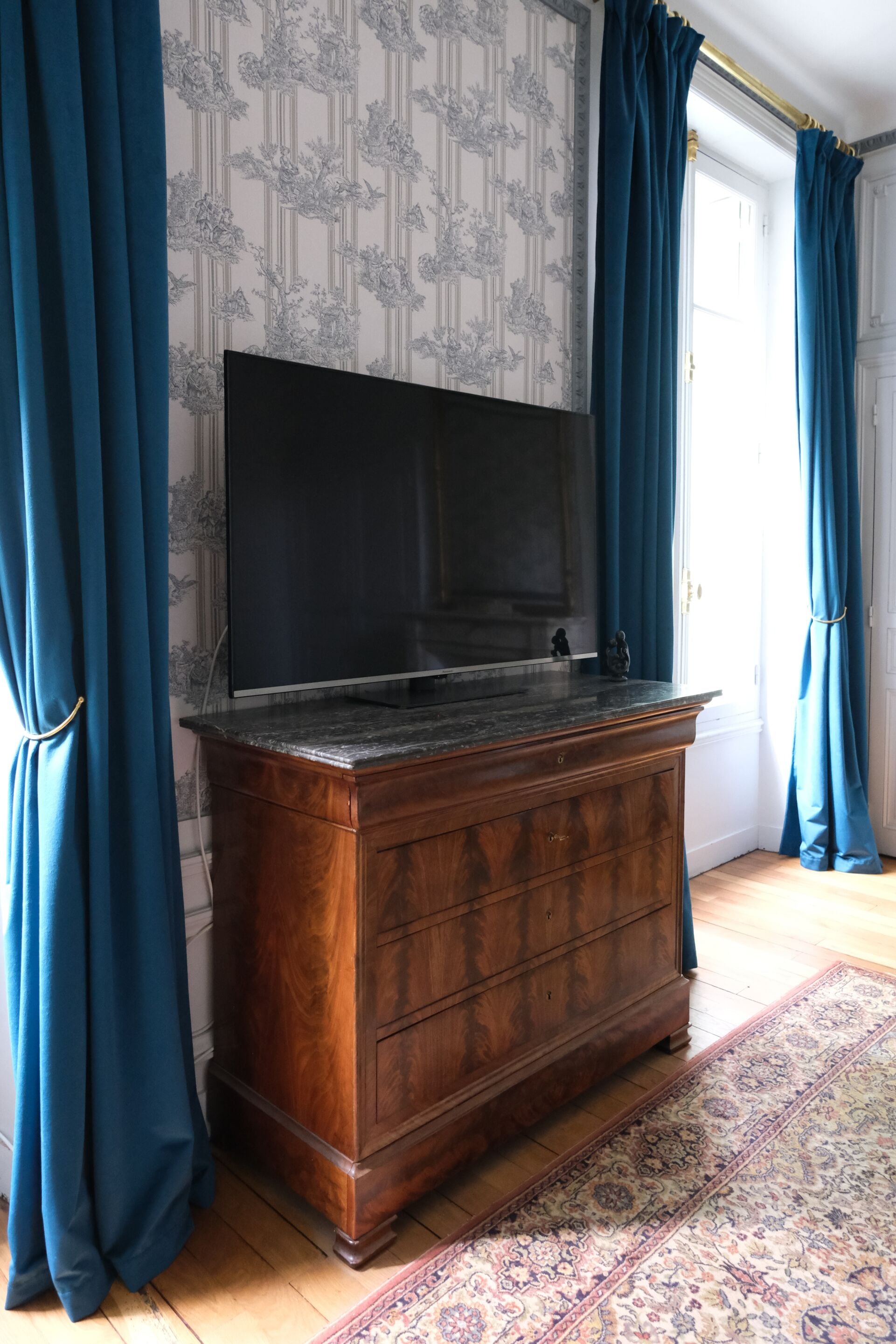 Una habitación con un mueble grande de madera, un televisor encima y cortinas azules.