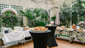 An outdoor buffet setup with various food items on tables, surrounded by greenery and a rustic stone wall. - Suite de l'Opéra  (Vichy)