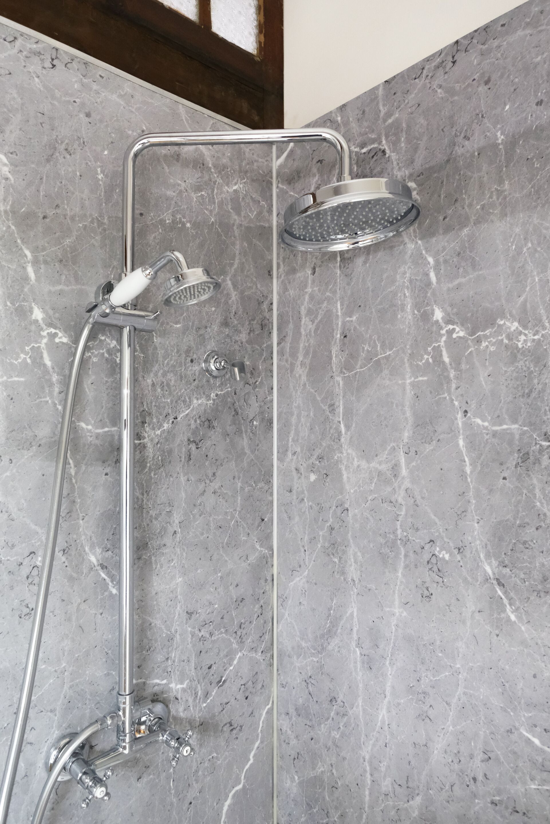 Ducha moderna con cabezal de ducha manual y cabezal de ducha fijo montado en una pared de mármol.