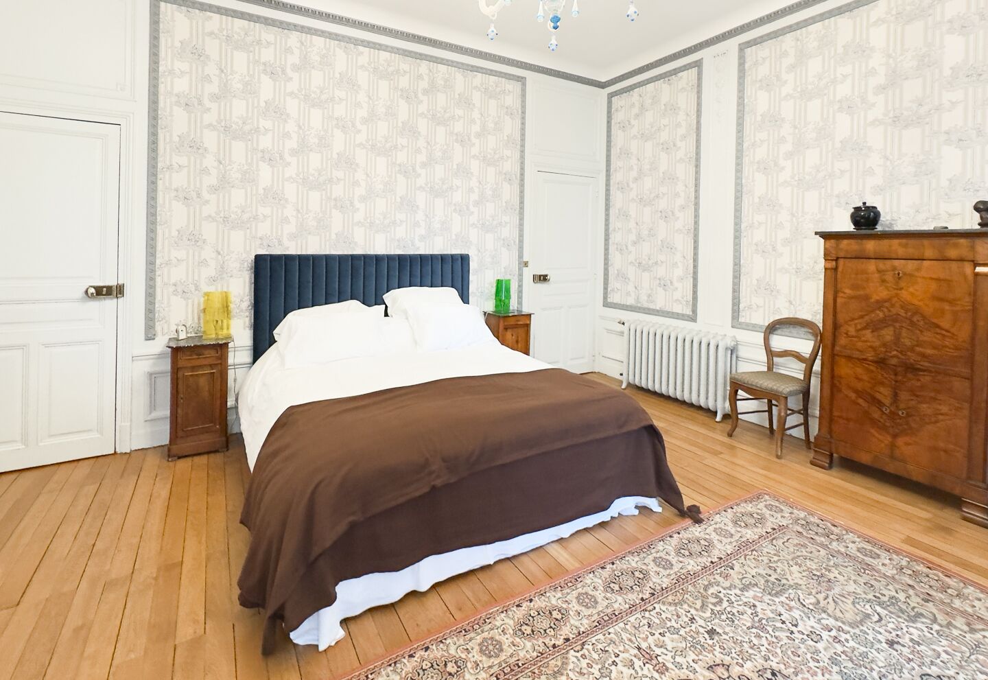 A bedroom with a bed, nightstands, a dresser, a chair, and a radiator.