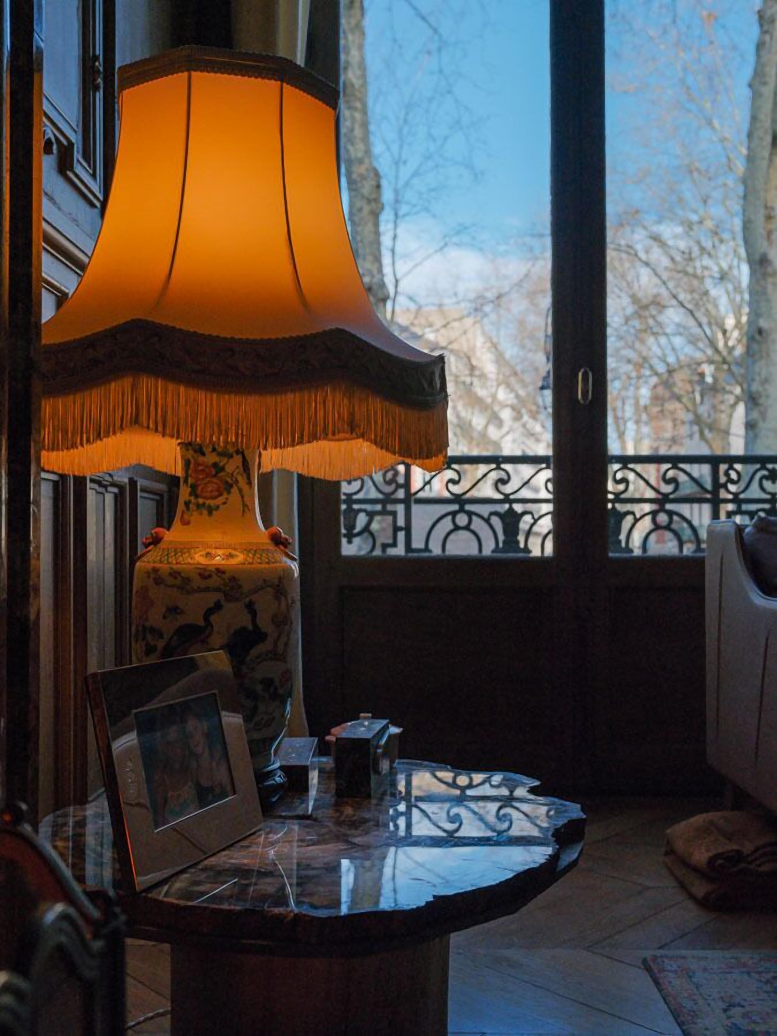 A room with a table, a lamp, and a view through a window.