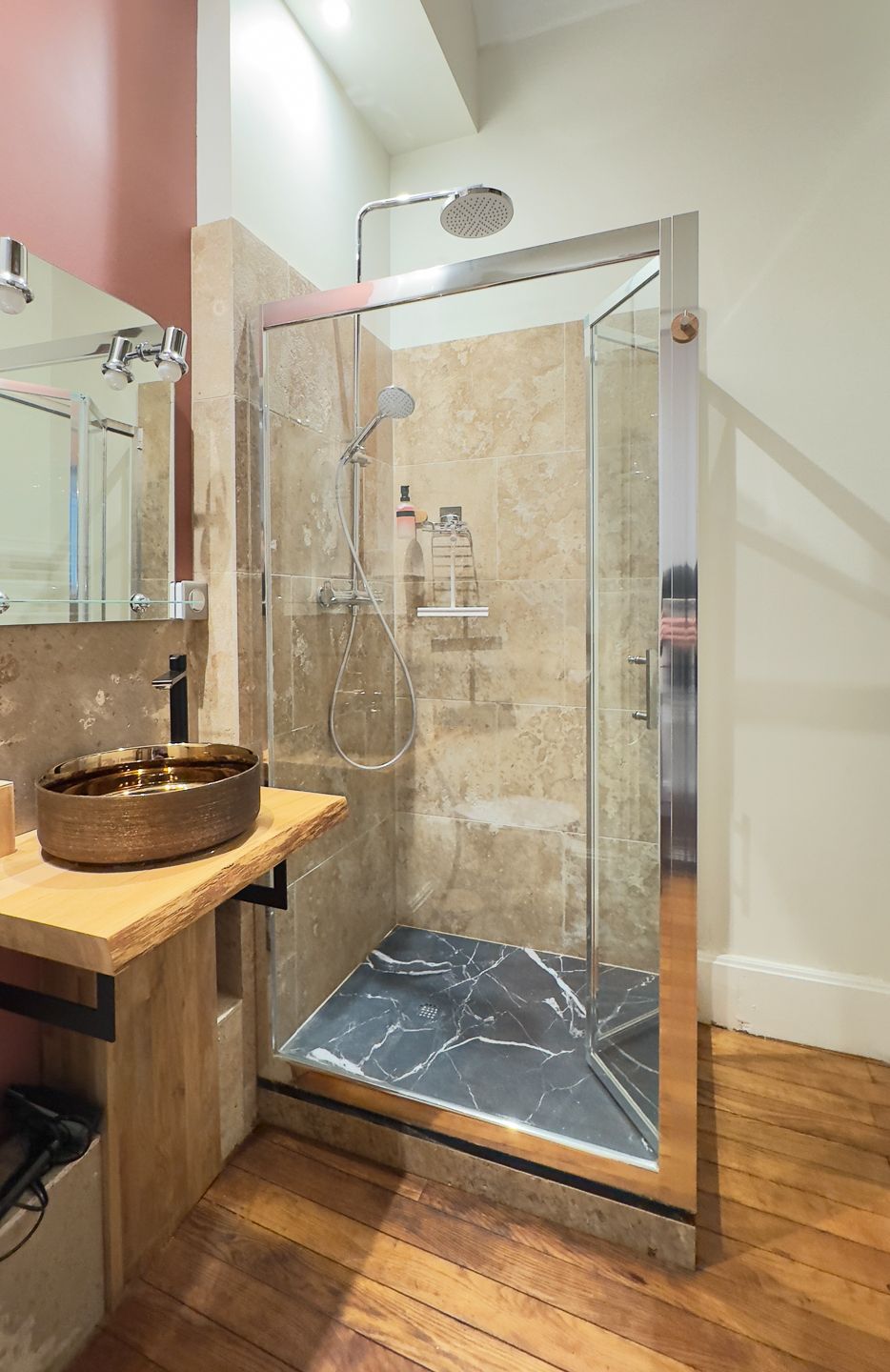 A modern bathroom with a glass-enclosed shower, a wooden vanity, and a marble-tiled floor.