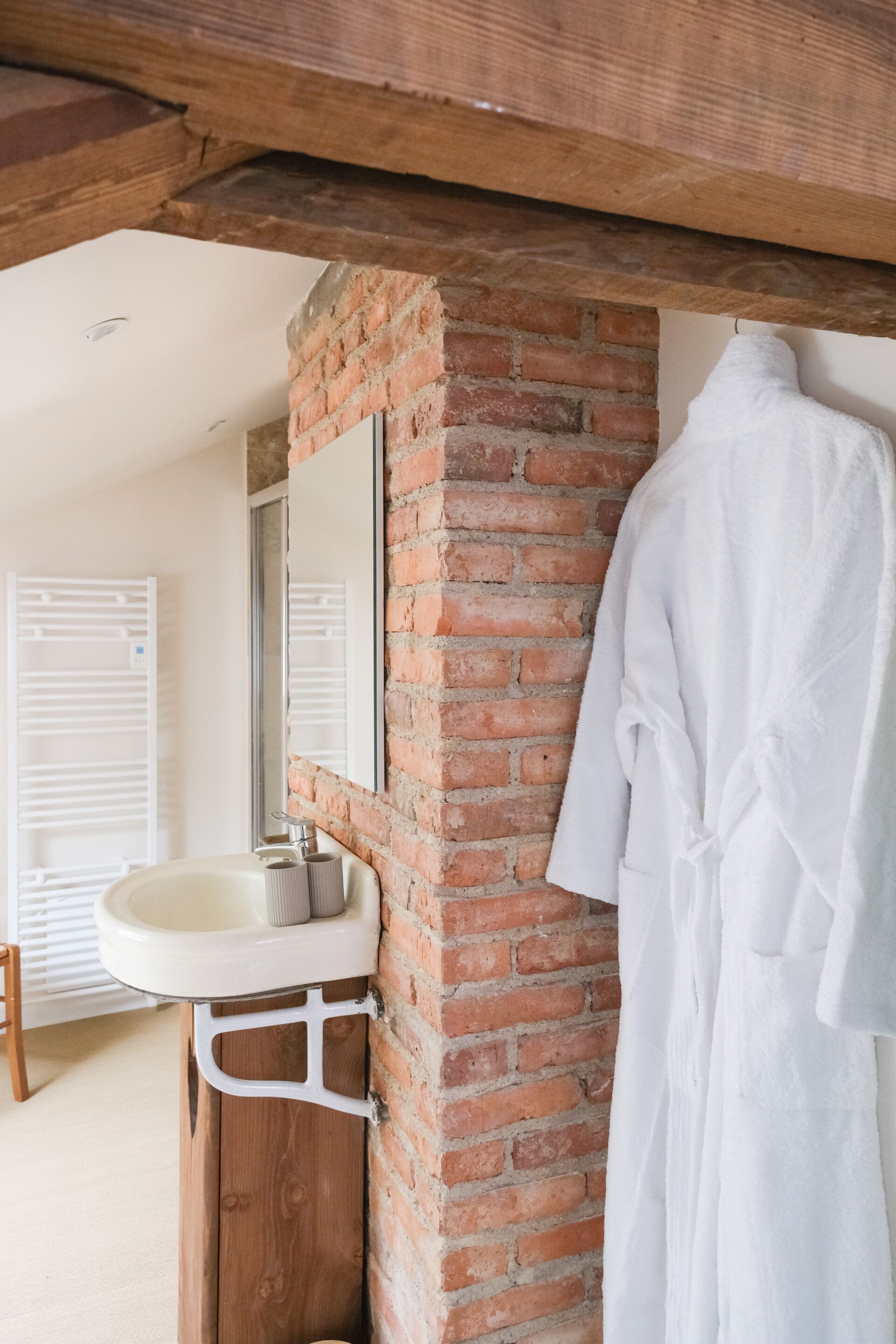 Ein Badezimmer mit einem weißen Waschbecken, einem Spiegel und einem weißen Bademantel, der an der Wand hängt.