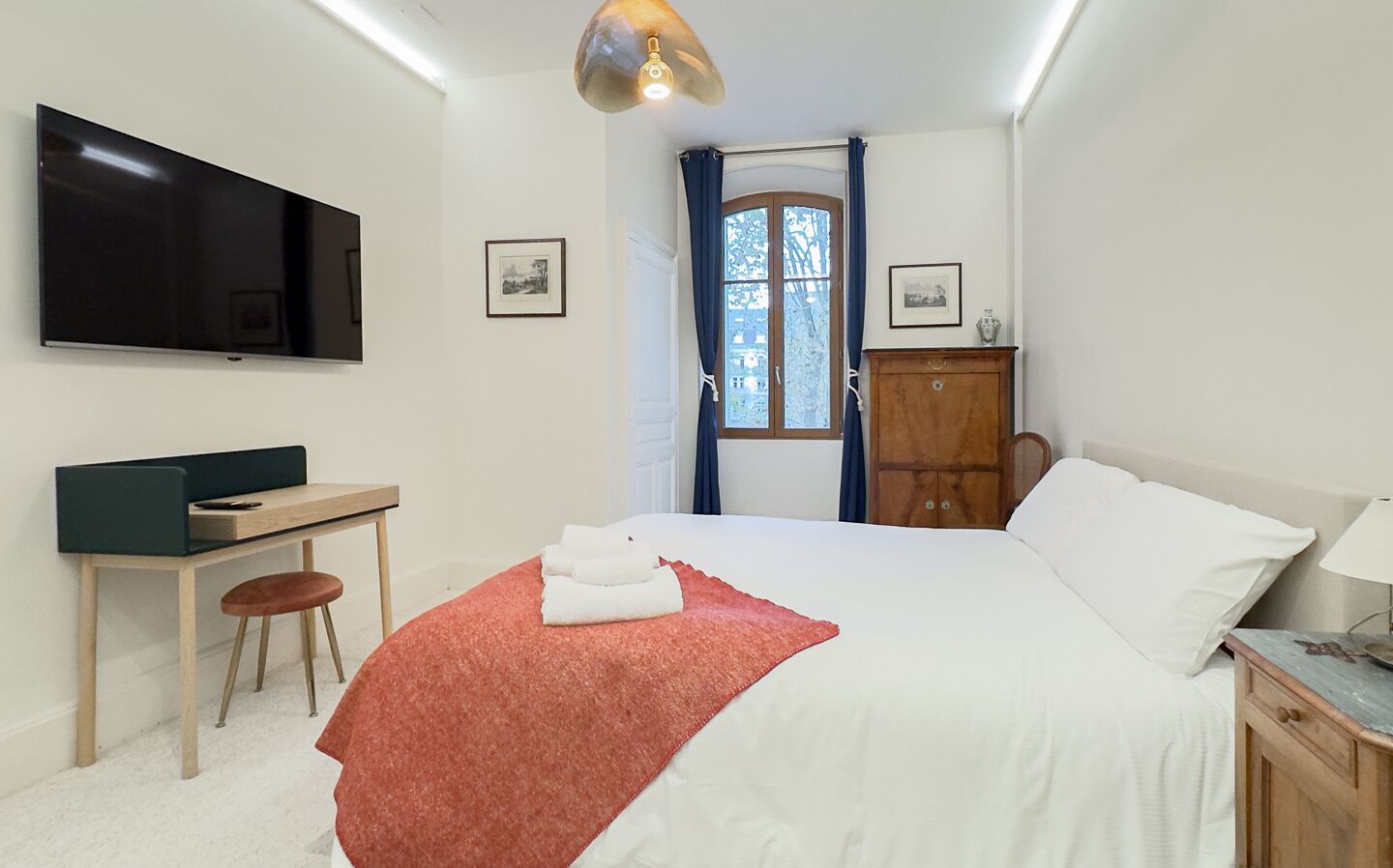 Quarto moderno com cama, escrivaninha, cadeira, televisão e guarda-roupa.