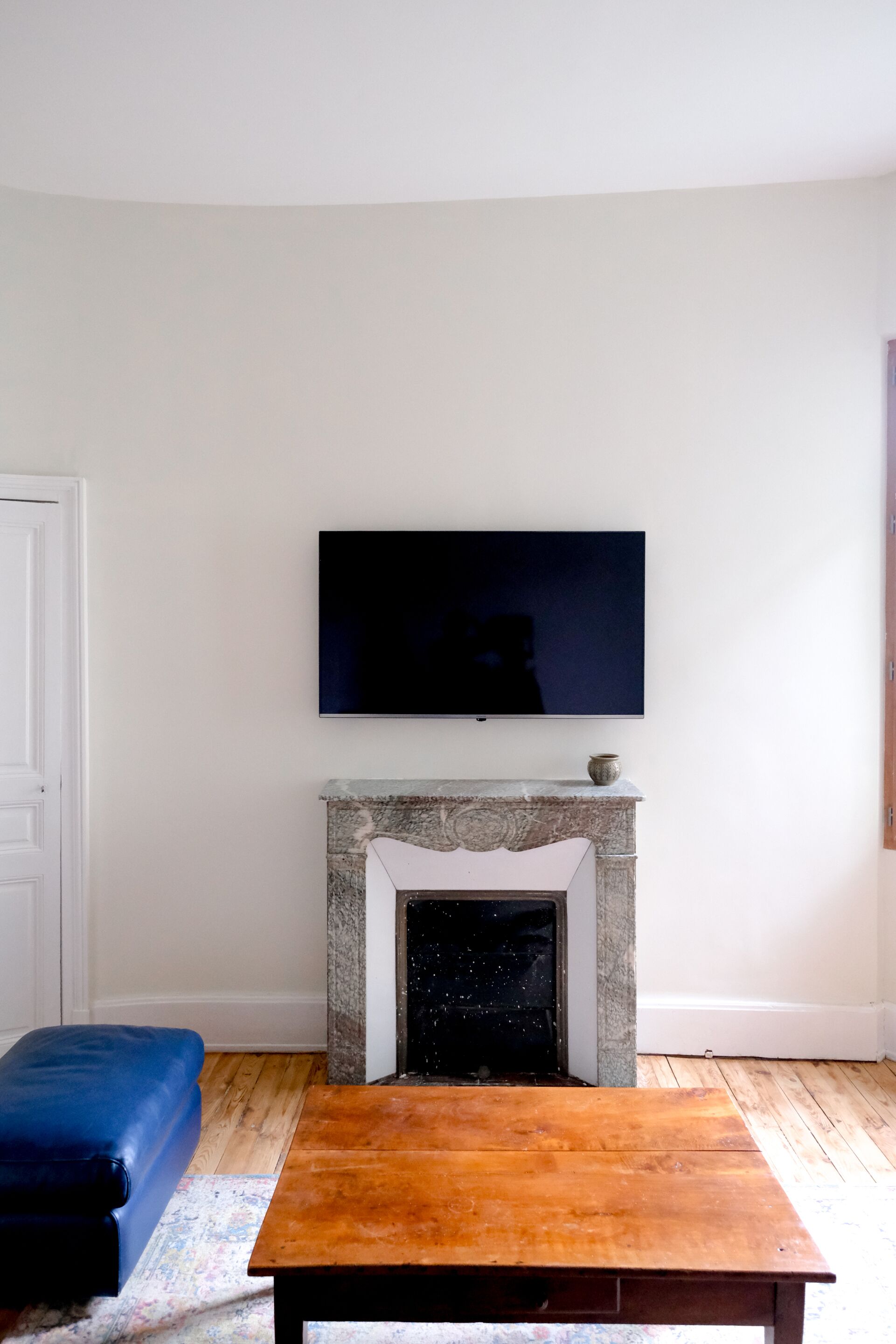 Habitación con una televisión sobre la chimenea, una mesa de madera en primer plano y un banco azul a la izquierda.