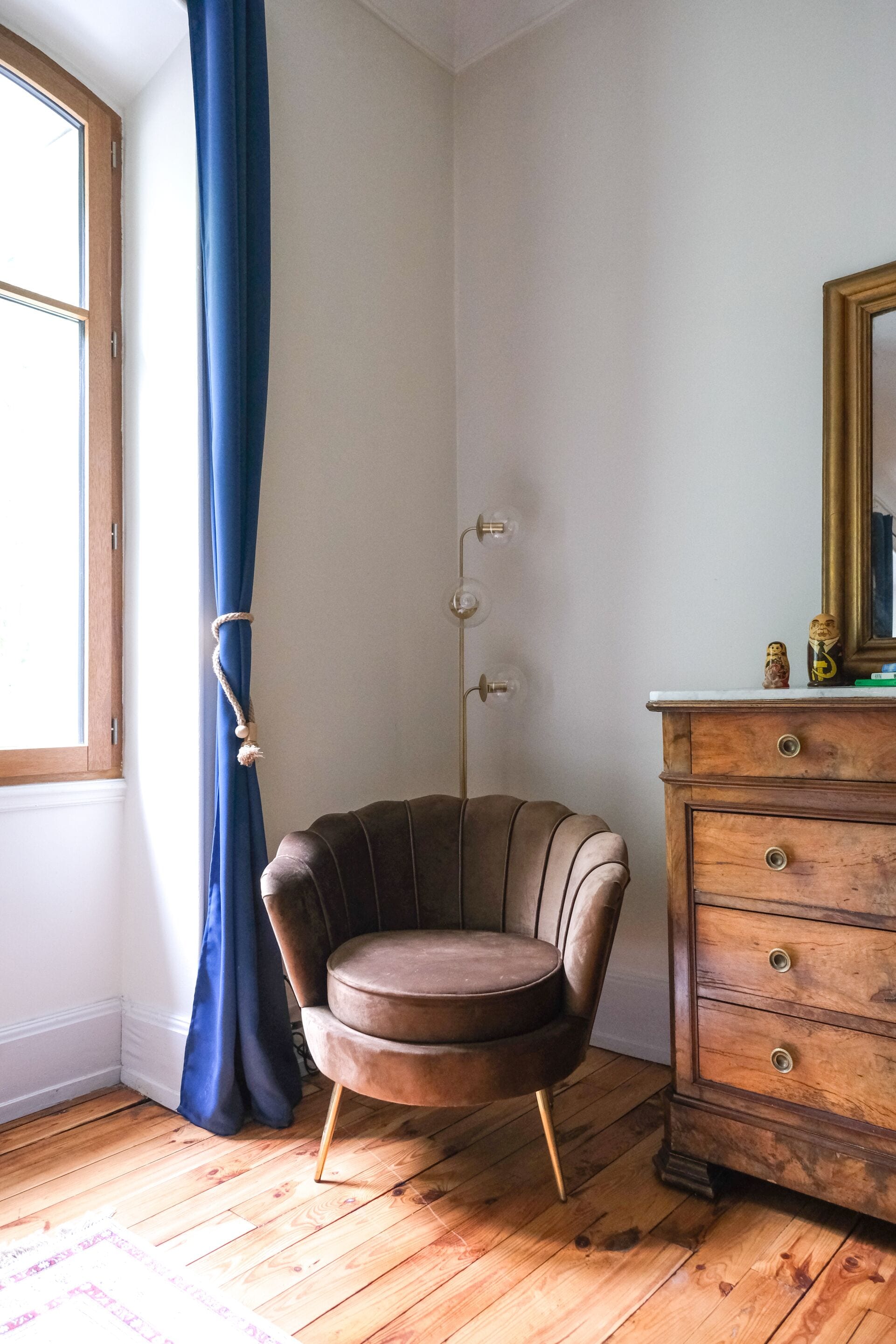 A room with a brown leather chair, a wooden dresser, and a window with blue curtains.