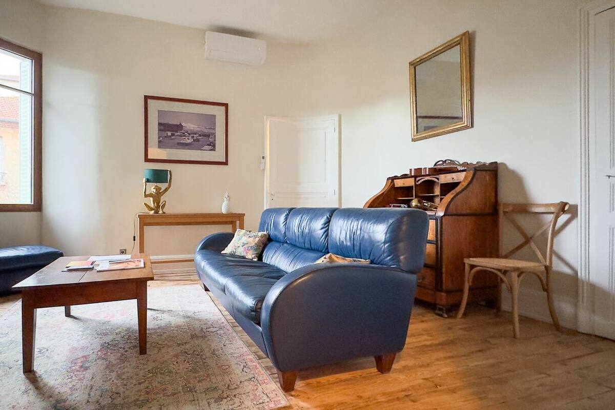 Una sala de estar con un sofá de cuero azul, una mesa de centro de madera, una mesita auxiliar de madera, un cuadro enmarcado en la pared y un ventanal grande.