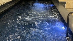 A spa pool with a textured wall, a glass partition, and a stone wall with a light fixture. - Suite de l'Opéra  (Vichy)