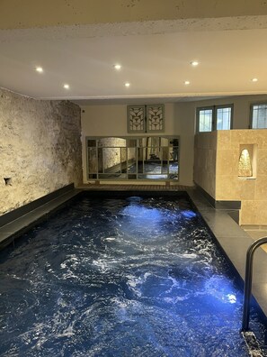 A spa pool with a textured wall, a glass partition, and a stone wall with a light fixture.