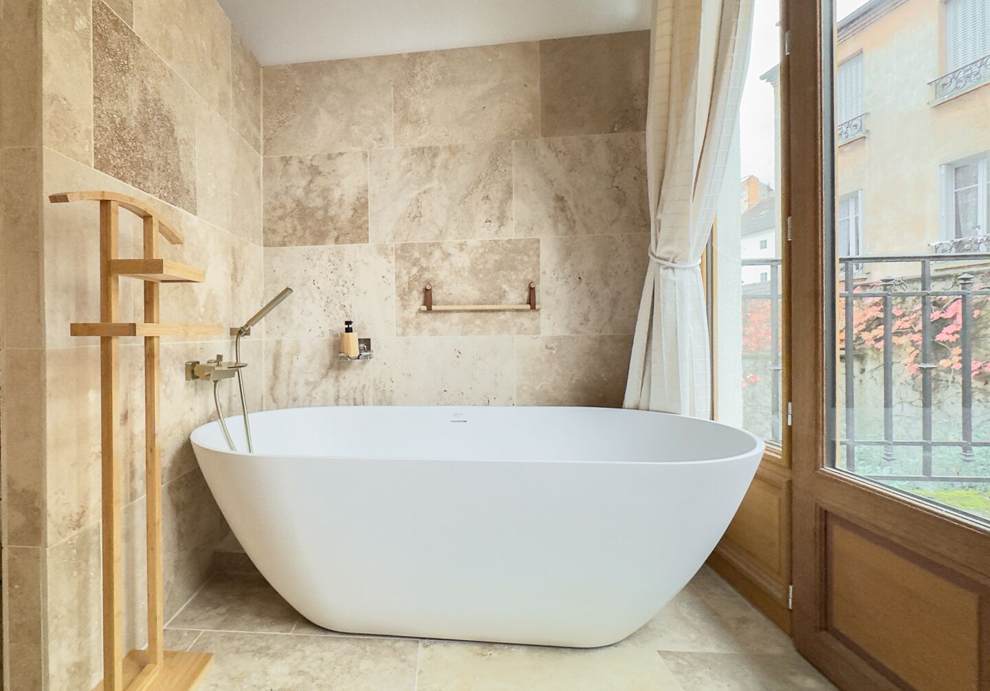 Une salle de bain moderne avec une baignoire sur pieds, une douche en bois et une vue sur un balcon doté d’une balustrade.