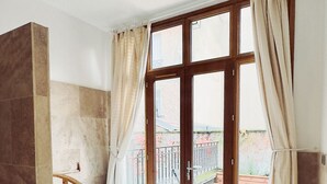 A bathroom with a bathtub, a wooden vanity, and a large window with curtains. - Suite de l'Opéra  (Vichy)