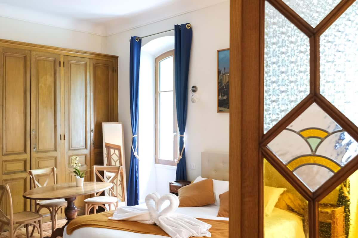 Un dormitorio con cama, un armario de madera, un escritorio con silla y una ventana con cortinas.